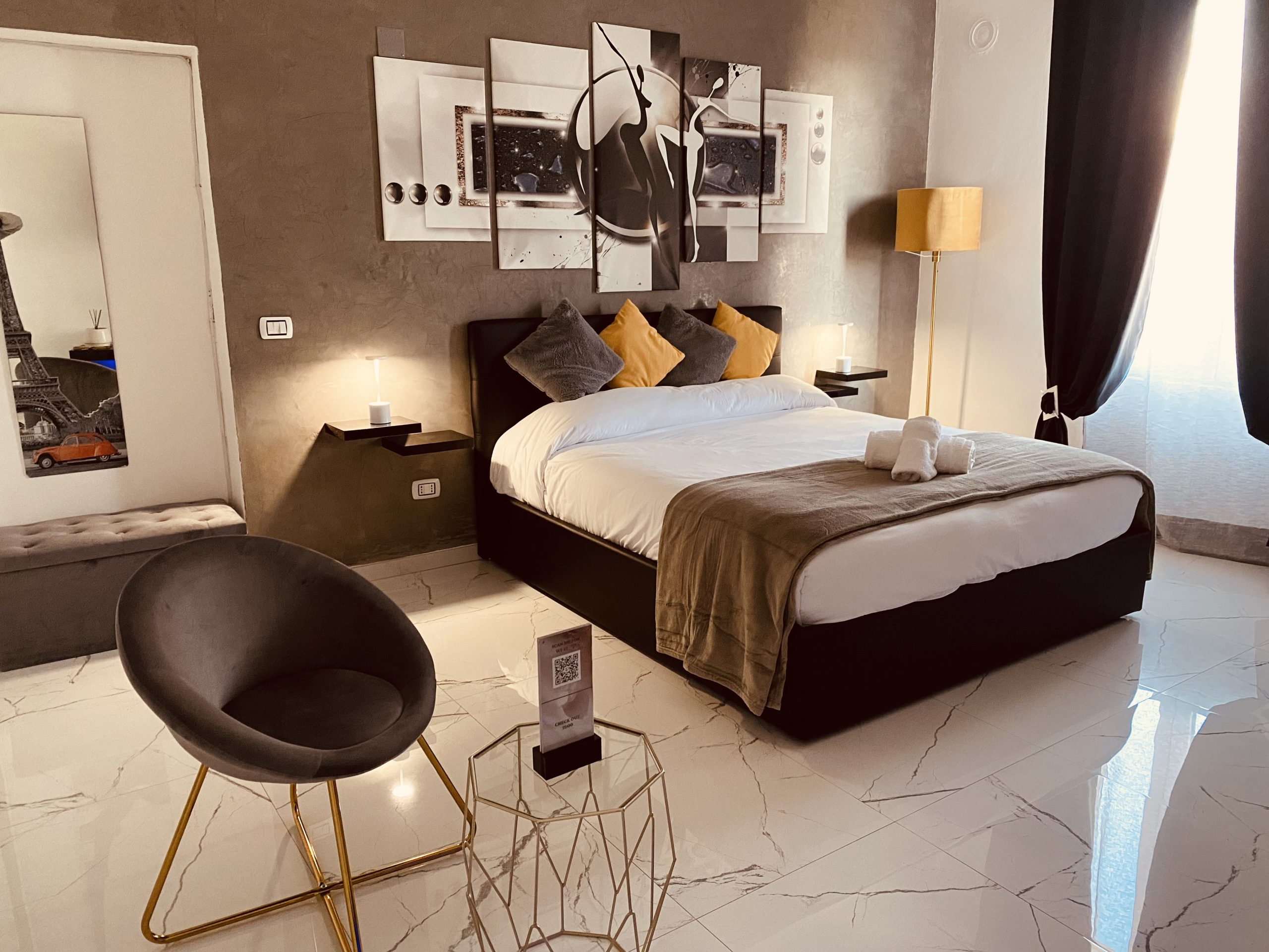 Dettaglio del letto king-size, dell'imponente quadro e dell'angolo relax con poltroncina e tavolino in una camera elegante del B&B G-House a Parma.